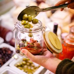 Glass jar being filled with olives and antipasti